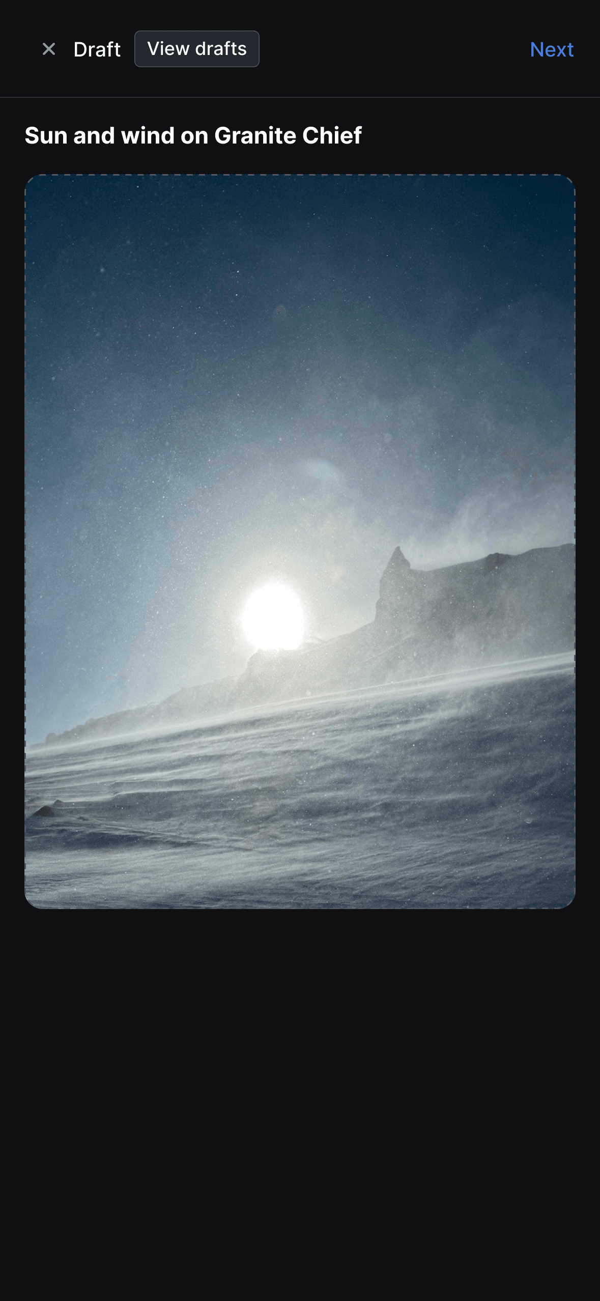 Draft post creation interface showing a landscape photograph titled "Wind and sun on Granite Chief." The image captures a dramatic mountain scene with bright sunlight breaking through clouds or fog along a mountainous horizon, illuminating what appears to be a snowy or misty foreground. Navigation options at the top include "Draft," "View drafts," and "Next" buttons against a dark background.